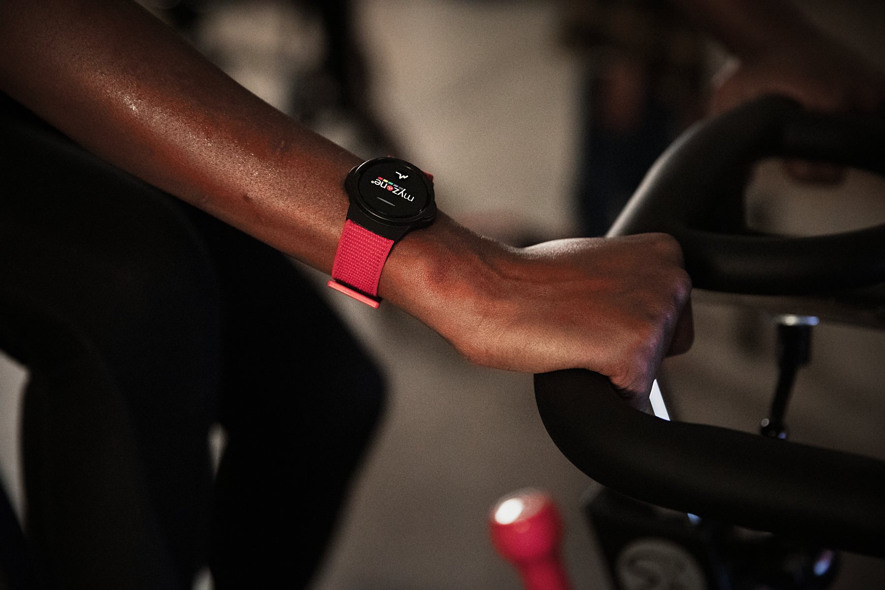 Arm wearing a Myzone heart rate monitor, holding on to an exercise bike