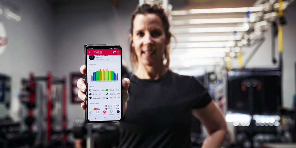 A woman showing the camera her workout, displayed on the Myzone app