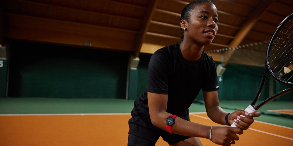 A woman holding a tennis racquet and wearing a heart rate monitor