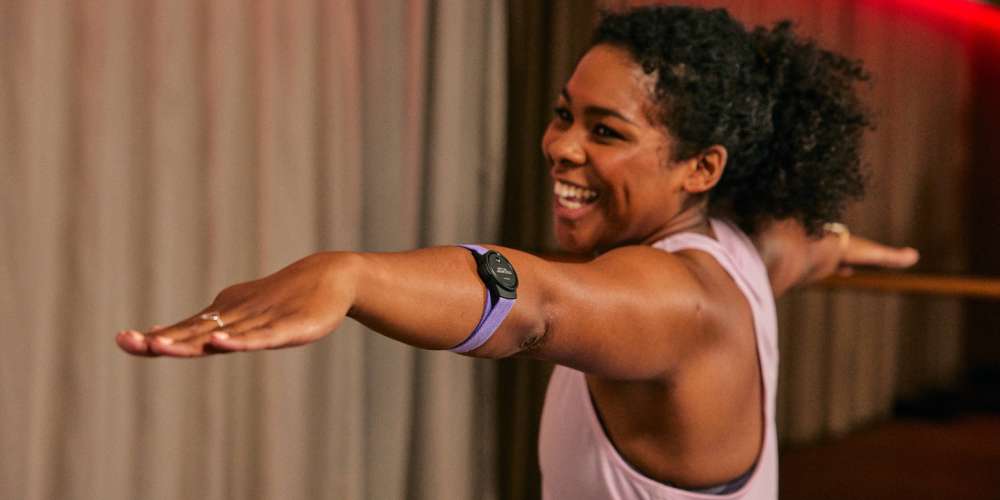 A woman standing in a yoga pose in an exercise studio, wearing a heart rate monitor