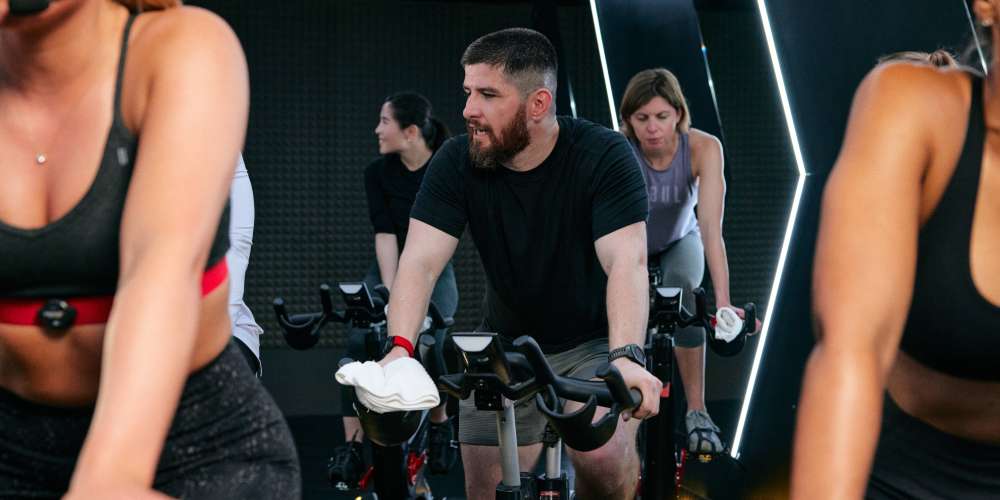 A man in the middle of a cycling studio class in a gym