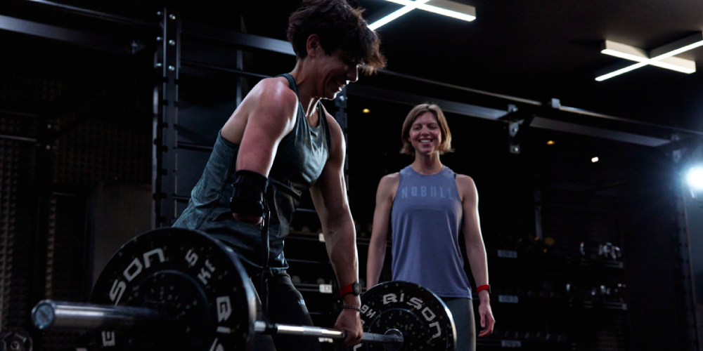 Paralympian Joana Calado lifting a barbell while British Champion swimmer Rebecca Guy watches