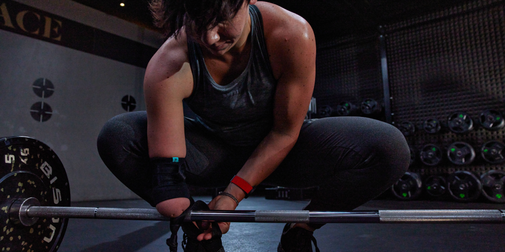 Paralympian Joana Calado attaching an adaptive athlete strap on to a barbell, wearing a heart rate monitor