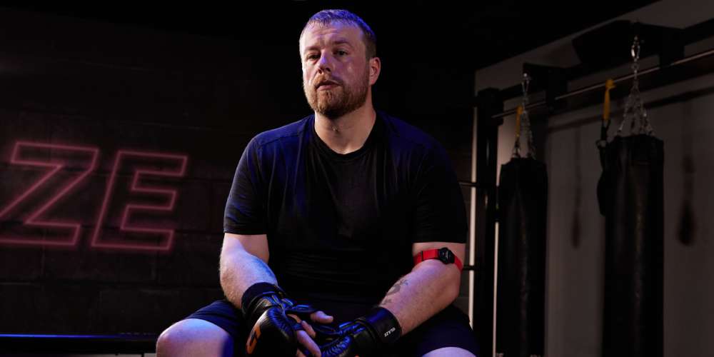 Man sitting in a fitness studio wearing MMA gloves and a heart rate monitor after a workout