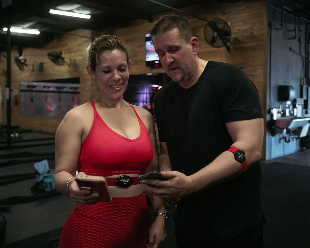 Woman and a man looking at smartphones wearing Myzone heart rate monitors