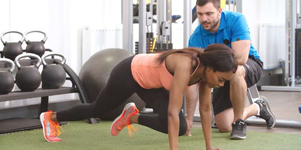 A woman doing bodyweight workouts in front of a personal trainer