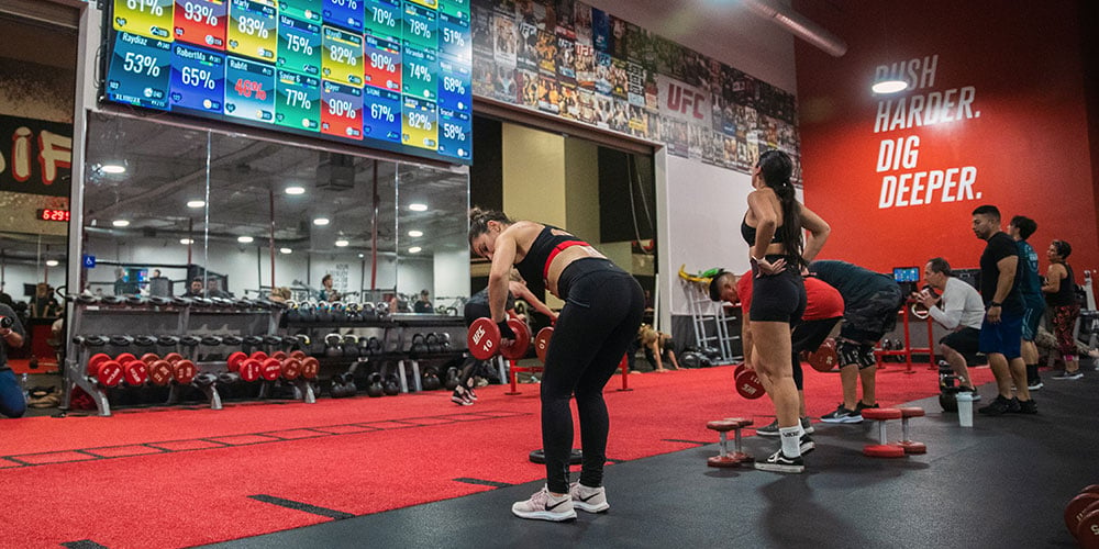 Gym members working out at UFC GYM in front of a Myzone screen