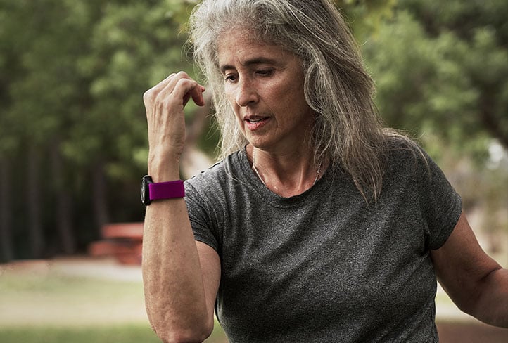 Older adult woman wearing a heart rate monitor, exercising outdoors in a park