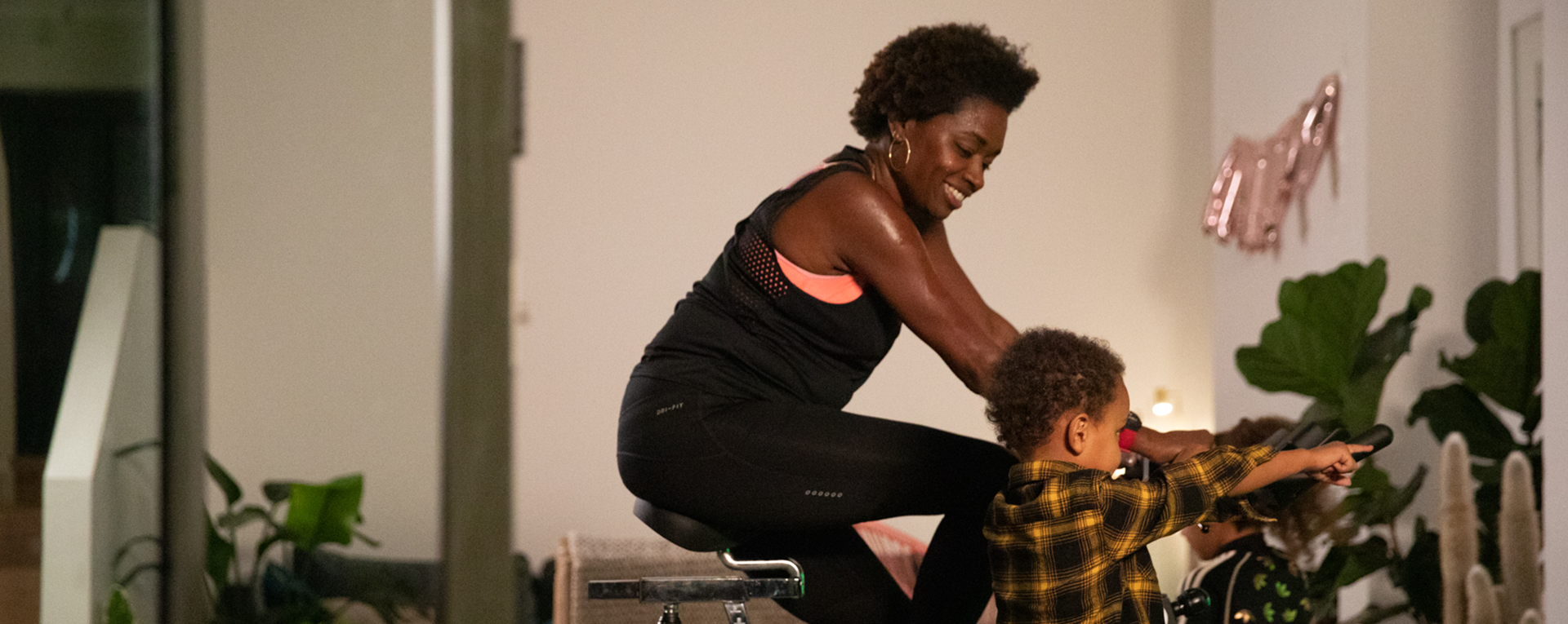 Woman on an exercise bike with a child watching