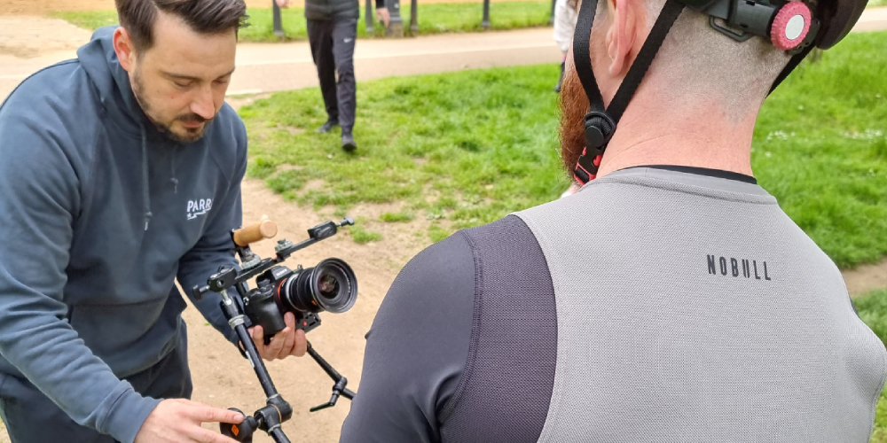 A videographer shooting a health and fitness video, focussed on a cyclist