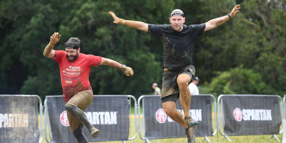 Two Myzone staff members jumping over the fire finish line on a Spartan Beast race