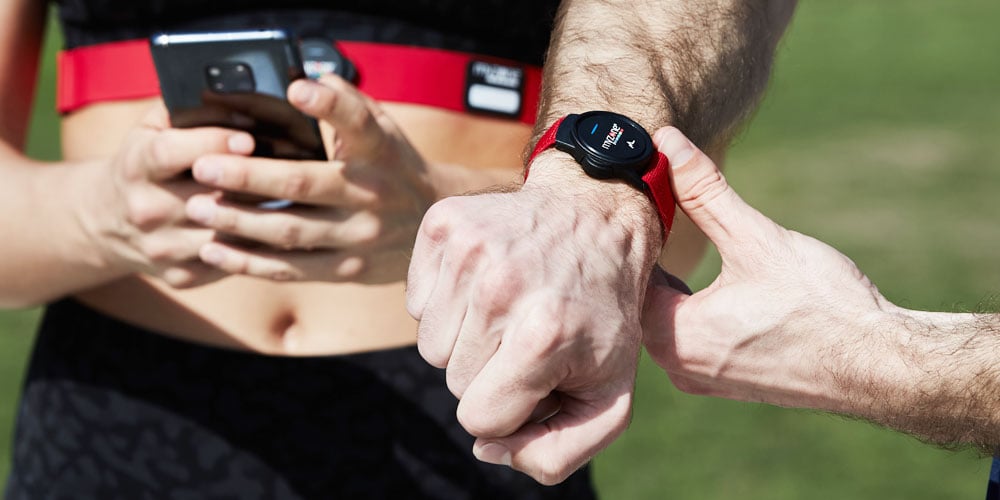 Two people wearing Myzone Switch heart rate monitors and looking at the Myzone app