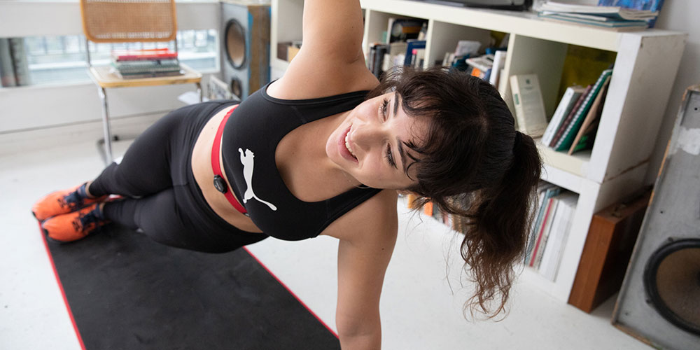 Woman working out at home holding a side plank, wearing a Myzone chest strap