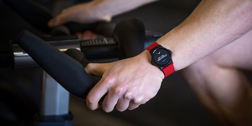 Person riding an indoor cycle in a fitness class, wearing a Myzone heart rate monitor