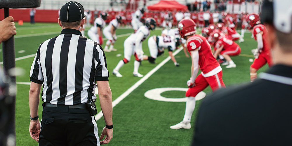 American football players lining up on the gridiron with a referee watching