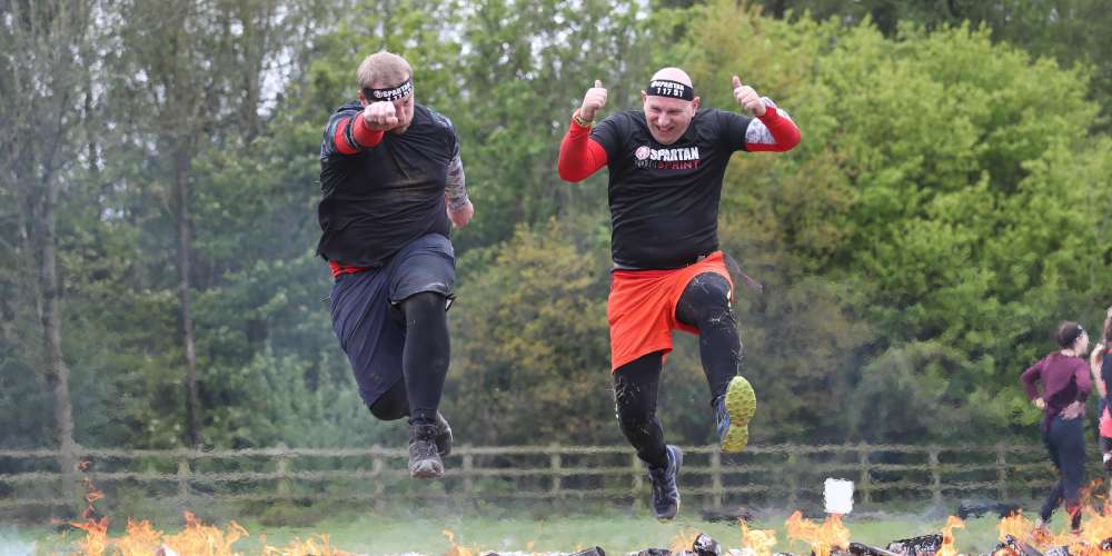 Two Spartan racers crossing the finish line together over the fire jump